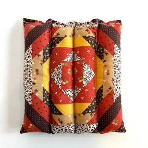 May include: A square, quilted cushion with a patchwork design. The cushion features a central diamond pattern in red, yellow, and white floral fabric, surrounded by diagonal stripes in various patterns and colours, including brown polka dots and floral prints.