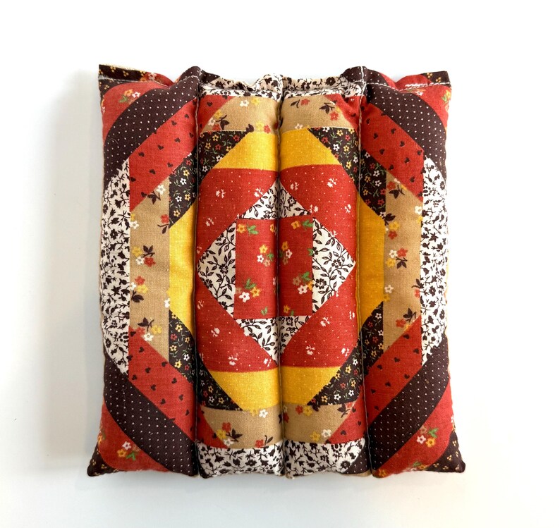 May include: A square, quilted cushion with a patchwork design. The cushion features a central diamond pattern in red, yellow, and white floral fabric, surrounded by diagonal stripes in various patterns and colours, including brown polka dots and floral prints.