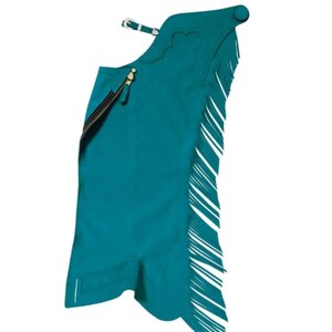 May include: Teal leather chaps with white fringe. The chaps feature a zip closure and a buckle fastening at the top. Designed for riding, they have a decorative scalloped edge. The chaps are approximately 100 cm in length.