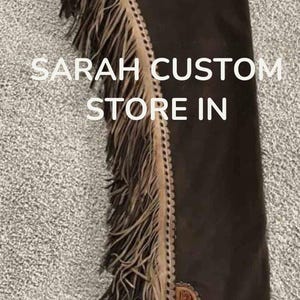 May include: Dark brown leather chaps with intricate floral and scroll tooling. The chaps feature long fringe along the sides and decorative accents. The text "SARAH CUSTOM STORE IN" is visible.