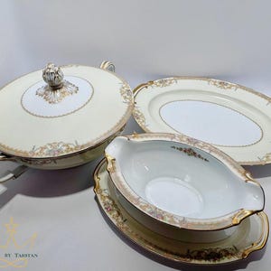 Puede incluir: Un juego de servir de porcelana color crema con ribetes dorados y detalles florales. El juego incluye una sopera con tapa, una fuente ovalada y una salsera con un plato a juego. La sopera tiene asas y un adorno decorativo.