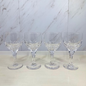 Peut inclure: Quatre verres à vin en cristal transparent avec un motif gravé sur le bol. Les verres ont une longue tige et une base ronde. Le fond est un mur à motifs de marbre blanc.
