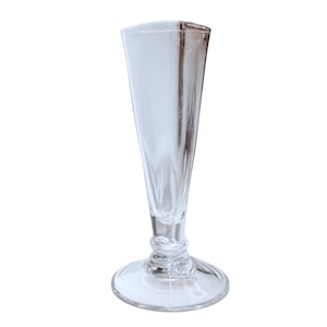 Puede incluir: Una copa de champán transparente con una parte superior acampanada de forma rectangular. El vaso tiene un cuerpo delgado y cónico y una base redondeada. El tallo presenta un diseño decorativo y acanalado. El vaso es de cristal transparente.