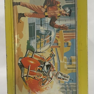 Puede incluir: Fiambrera met&aacute;lica vintage con marco amarillo e ilustraci&oacute;n retro de ciencia ficci&oacute;n. La obra de arte representa a un hombre con traje espacial y una ciudad futurista con una nave espacial. La fiambrera tiene tapa con bisagras y cierre met&aacute;lico.