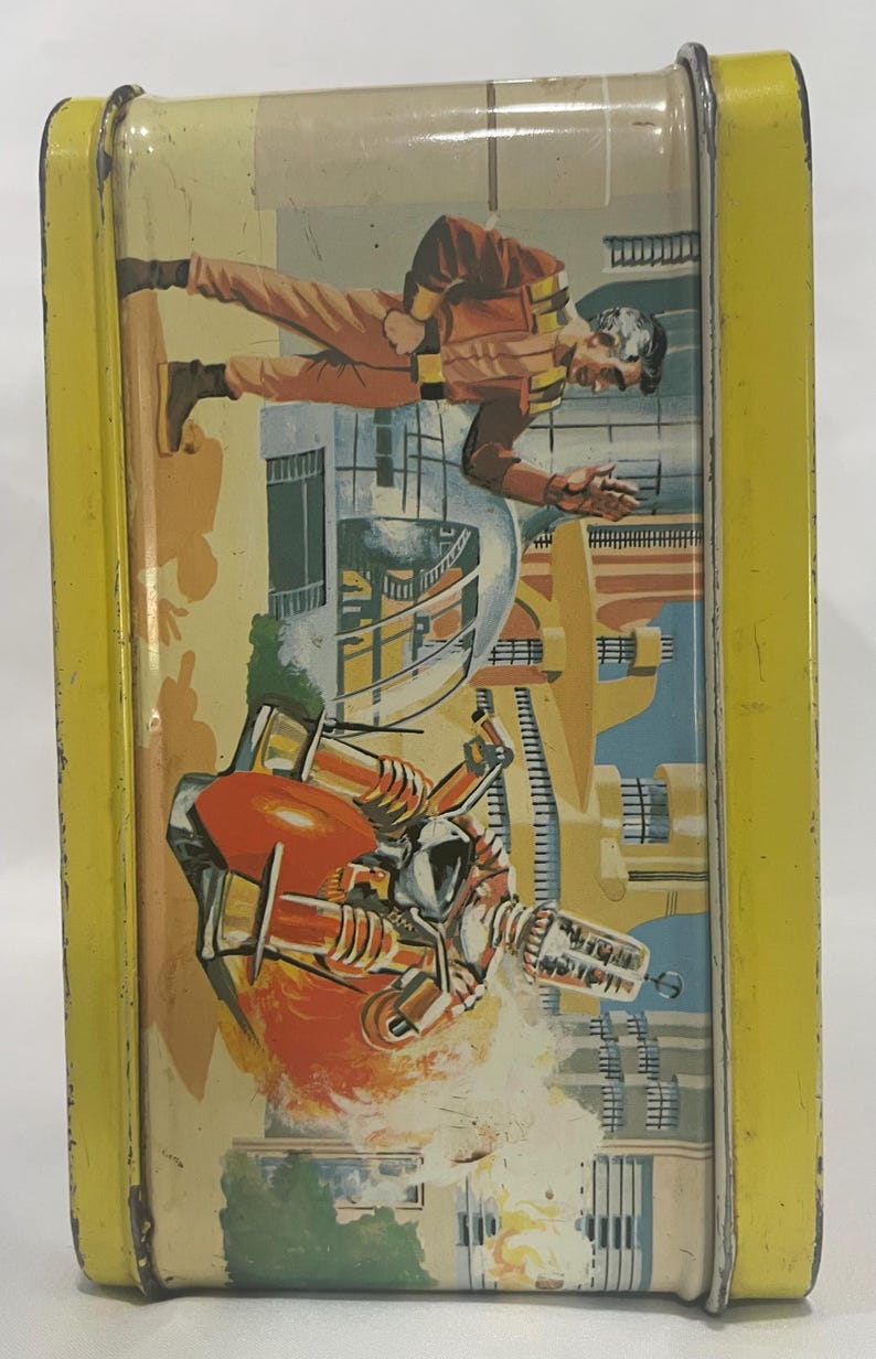Puede incluir: Fiambrera met&aacute;lica vintage con marco amarillo e ilustraci&oacute;n retro de ciencia ficci&oacute;n. La obra de arte representa a un hombre con traje espacial y una ciudad futurista con una nave espacial. La fiambrera tiene tapa con bisagras y cierre met&aacute;lico.