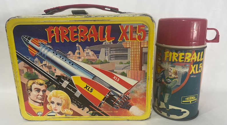 Puede incluir: Juego vintage de fiambrera y termo Fireball XL5. La fiambrera es amarilla con asa roja y presenta un gr&aacute;fico de cohete. El termo es granate y verde azulado con un gr&aacute;fico a juego. Un coleccionable retro.
