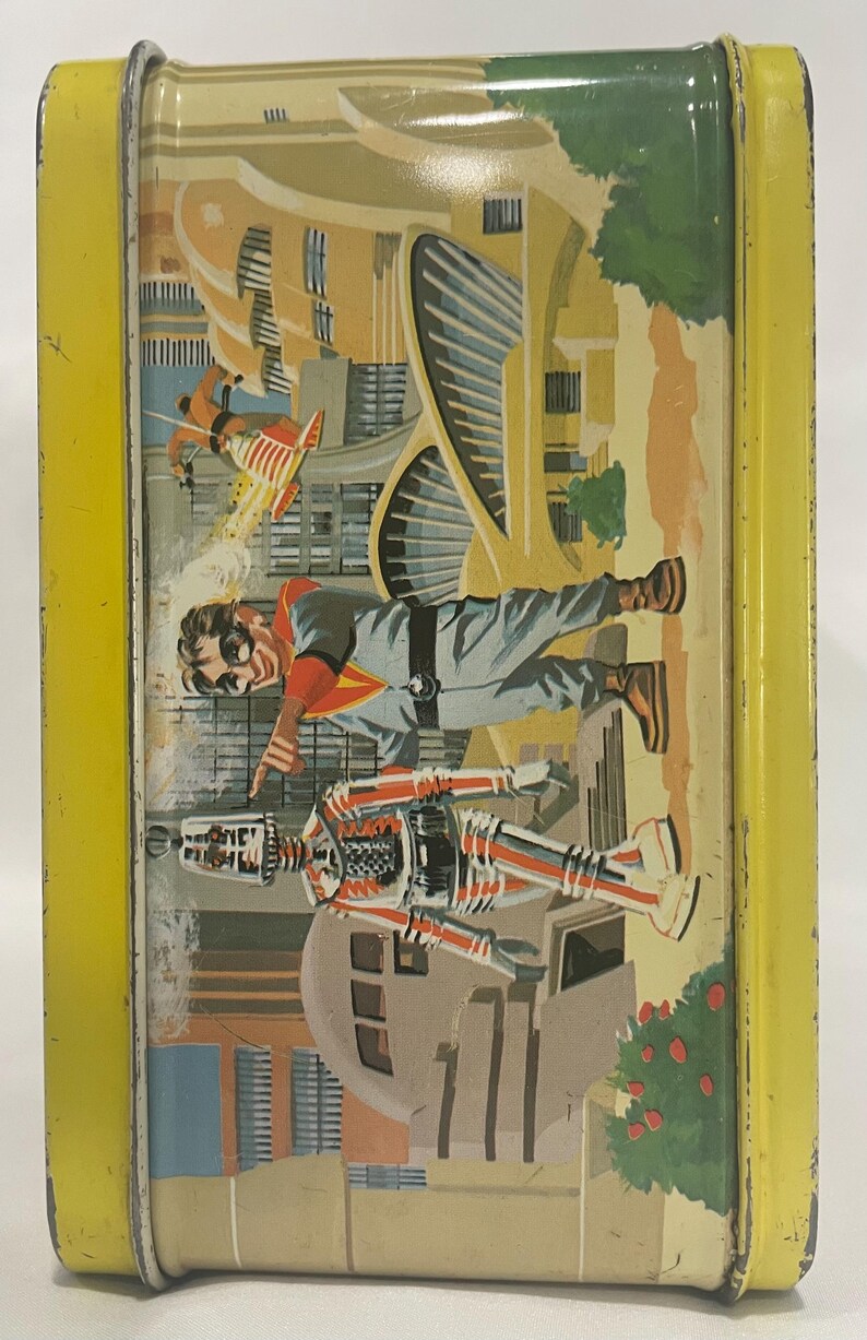 Puede incluir: Fiambrera met&aacute;lica vintage con borde amarillo. La ilustraci&oacute;n representa un paisaje urbano futurista con un hombre con mono gris y un robot. Una persona con un jetpack vuela en el fondo. La fiambrera tiene un dise&ntilde;o retro de mediados de siglo.