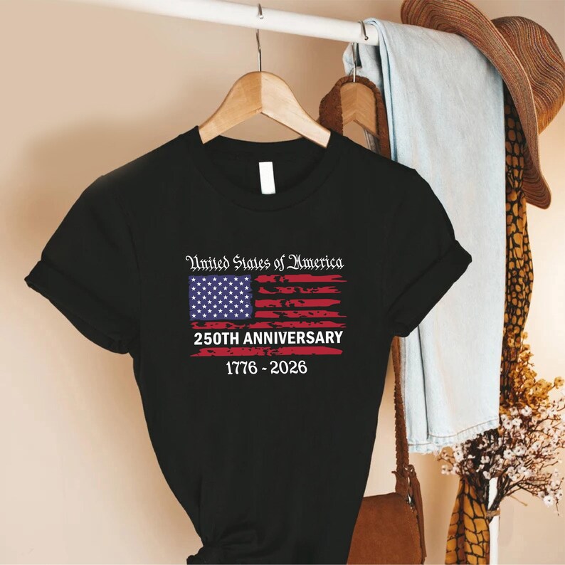 May include: Black t-shirt featuring a graphic of the American flag with the text "United States of America 250th Anniversary 1776-2026". The design includes a blue rectangle with white stars and red and white stripes.