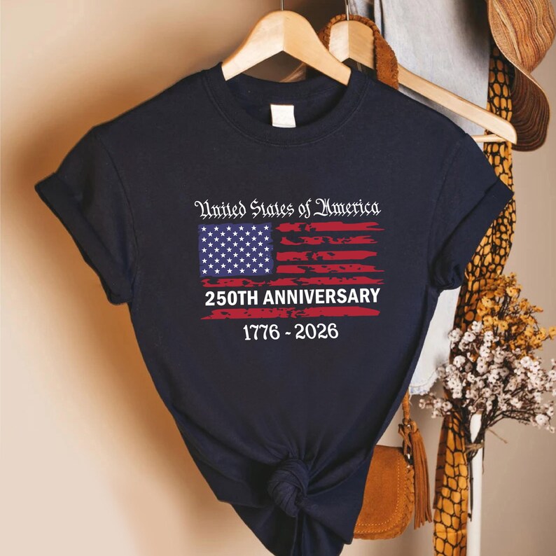 May include: Navy blue t-shirt featuring the American flag design with the text "United States of America 250th Anniversary 1776-2026". The flag design includes stars and stripes in red, white, and blue.