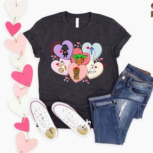 May include: Dark gray t-shirt featuring a heart-shaped graphic with Star Wars characters. The shirt is paired with blue jeans and white sneakers. Decorative pink and white heart garland is on the left. The text "CUSTOM RANDOM Gifts" is in the upper right.