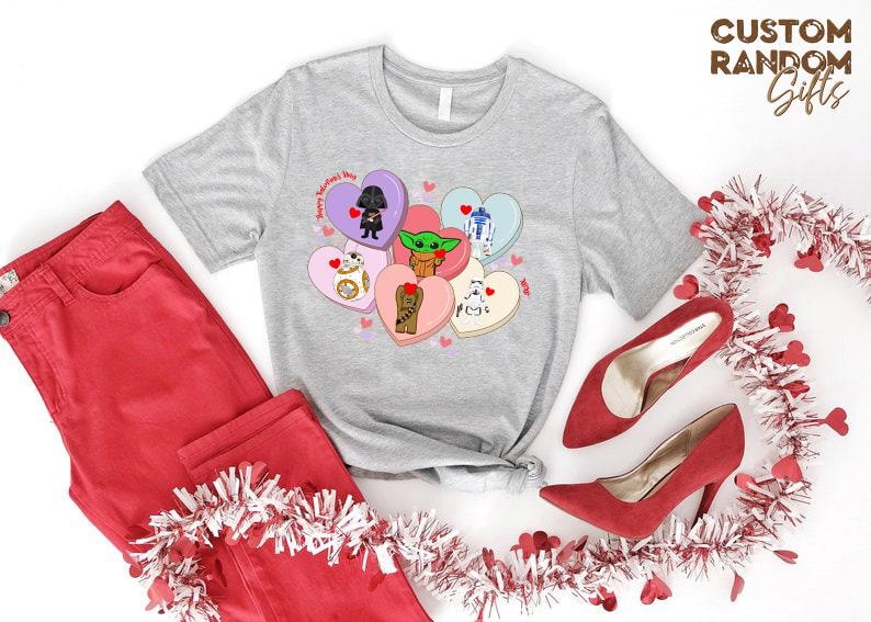 May include: A light gray t-shirt featuring a design of Star Wars characters on heart-shaped candies. The shirt is paired with red pants and red high heels. The text "Happy Valentine's Day" is on the shirt.
