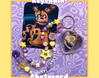 May include: A keychain featuring a heart-shaped acrylic charm with a character illustration, attached to a beaded strand with yellow and purple star-shaped beads, round beads, and letter beads spelling SPRING BONNIE, plus a character photocard.