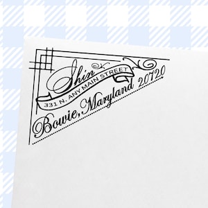 May include: Black and white address stamp with the name "Shin" in elegant script. The design includes the address "331 N. Any Main Street, Bowie, Maryland 20720" in a decorative banner and border. The stamp is on a white background.