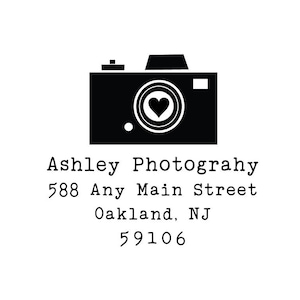 May include: Black and white image of a camera with a heart in the viewfinder. The text below reads "Ashley Photography", "588 Any Main Street", "Oakland, NJ", and "59106".