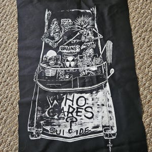 May include: Black graphic print on fabric featuring a car filled with zombie-like figures. The text "WAY OF LIFE" and "BRAINS" are visible. The phrase "WHO CARES? SUICIDE" is printed at the bottom of the car.