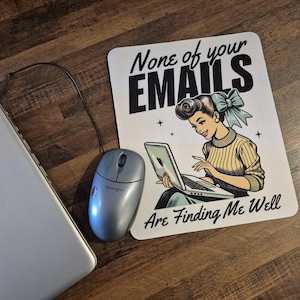 May include: A computer mouse and a mousepad with the text "None of your EMAILS Are Finding Me Well". The mousepad features a retro illustration of a woman using a laptop.