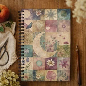 Puede incluir: Cuaderno de espiral con un diseño de patchwork colorido con lunas, flores y elementos botánicos. La portada tiene una estética suave de acuarela con una variedad de colores pastel. El cuaderno está sobre una superficie de madera.