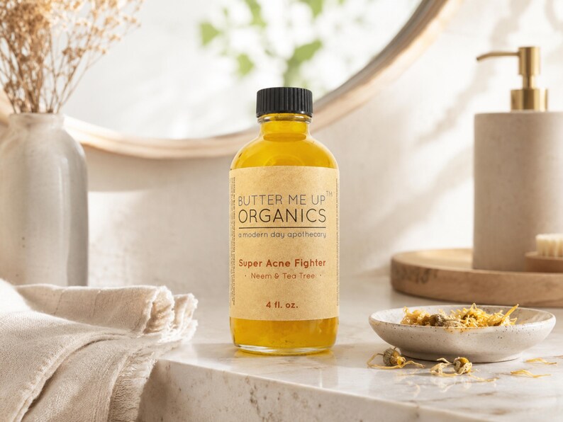 May include: A clear glass bottle with a black cap and a tan label that reads "BUTTER ME UP ORGANICS" and "Super Acne Fighter." The bottle contains a yellow liquid and is 4 fl. oz. A small ceramic dish with dried flowers sits nearby.