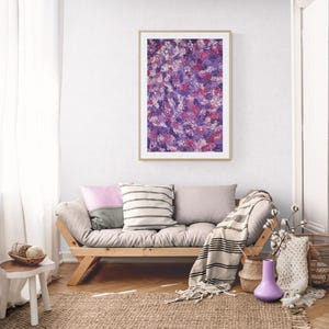 Puede incluir: Impresión artística abstracta en un marco de madera, con pinceladas moradas, rosas y blancas. La obra de arte cuelga sobre un sofá de madera con cojines y una manta a rayas. Una alfombra tejida y objetos decorativos completan la escena.