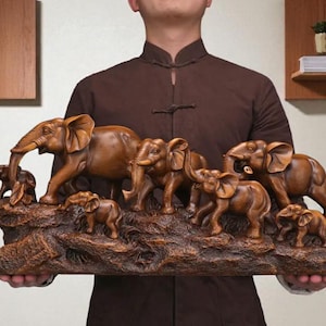 May include: A wooden sculpture of a herd of elephants, including adults and calves, carved from a single piece of wood. The elephants are arranged on a textured base, showcasing detailed craftsmanship and a natural wood grain.