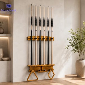 May include: A wall-mounted wooden pool cue rack holding six billiard cues with black and natural wood shafts. The rack features a top support bar with clips, a bottom shelf with two small drawers, and two hanging frames for billiard ball racks.