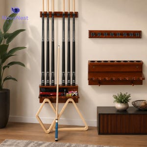 May include: A wall-mounted wooden pool cue rack holding six black and light wood cues, with a shelf for accessories, two wooden ball racks, and a separate wall-mounted rack with hooks. A single pool cue stands upright in the foreground.