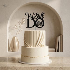 Pode incluir: Um bolo branco de dois andares com uma camada superior canelada e uma camada inferior lisa com acabamento dourado. Um topo de bolo preto está posicionado no topo com o texto We Still DO Since 1995 em estilo decorativo e negrito.
