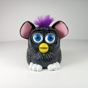 May include: A set of three ceramic mugs with a speckled, matte finish. The mugs are in shades of cream, light gray, and dark gray. Each mug has a simple, minimalist design and a rounded handle.