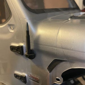 Puede incluir: Un modelo de Jeep plateado con detalles en negro, incluyendo una antena y manijas de puerta negras. El modelo Jeep tiene una rejilla de ventilación negra y una pegatina con el logotipo de Jeep. El vehículo es una réplica detallada.