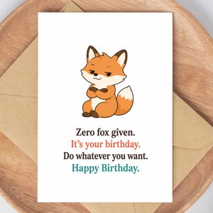 May include: A white greeting card featuring a cartoon fox with crossed arms and the text: Zero fox given. It's your birthday. Do whatever you want. Happy Birthday. The card is placed on a brown kraft paper envelope.