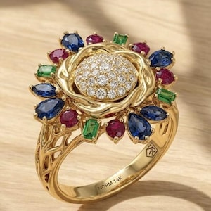 Pode incluir: Um anel de ouro 14K com um grupo central de diamantes em pavé, rodeado por um halo de safiras azuis em forma de pera, rubis redondos e pedras verdes em corte esmeralda. O aro tem um design intrincado e está marcado como NORM 14K.