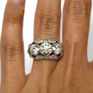 May include: A platinum ring featuring three large, round-cut diamonds set in a row, with smaller diamonds accenting the band. The ring is a classic design, showcasing brilliant sparkle and a timeless aesthetic.