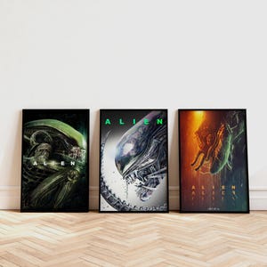 May include: Three framed Alien film posters. The posters depict images of the Alien creature in shades of green, black, and orange. The word "ALIEN" is printed in a bold font on each poster.