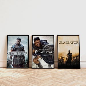 Könnte beinhalten: Drei gerahmte Filmplakate für den Film "Gladiator" werden gezeigt. Die Plakate zeigen Russell Crowe und andere Schauspieler in Actionposen, wobei der Filmtitel deutlich zu sehen ist. Die Plakate sind in schwarzen Rahmen.
