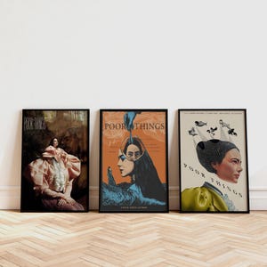 May include: Three framed movie posters titled "Poor Things". The posters showcase diverse artistic designs, including portraits and illustrations, with a range of colours like orange, blue, and pink. The posters are displayed on a wooden floor.