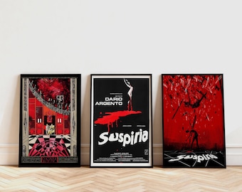 Puede incluir: Tres pósteres de película enmarcados de Suspiria. El póster izquierdo muestra un interior rojo con una escalera. El central presenta una silueta sobre una forma roja con el texto Dario Argento Suspiria. El derecho muestra una escena roja.