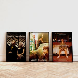 May include: Three framed posters for the film "Lost in Translation" are shown. The posters feature images of Bill Murray and Scarlett Johansson, cityscapes, and the film's title. The posters are in black frames and are displayed on a light wood floor.