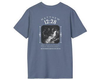 May include: A blue t-shirt with the text "MATTHEW 12:28" and a framed religious image. The text below the image reads "BUT IF IT IS BY THE SPIRIT OF GOD THAT I CAST OUT DEMONS THEN THE KINGDOM OF GOD HAS COME UPON YOU."