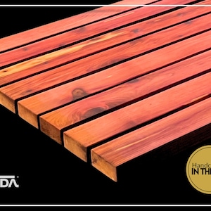 May include: A series of parallel, reddish-brown cedar wood slats arranged horizontally. The wood features visible natural grain patterns and knots. A logo with the text VIDA and a circular gold seal stating Handcrafted IN THE USA are visible.
