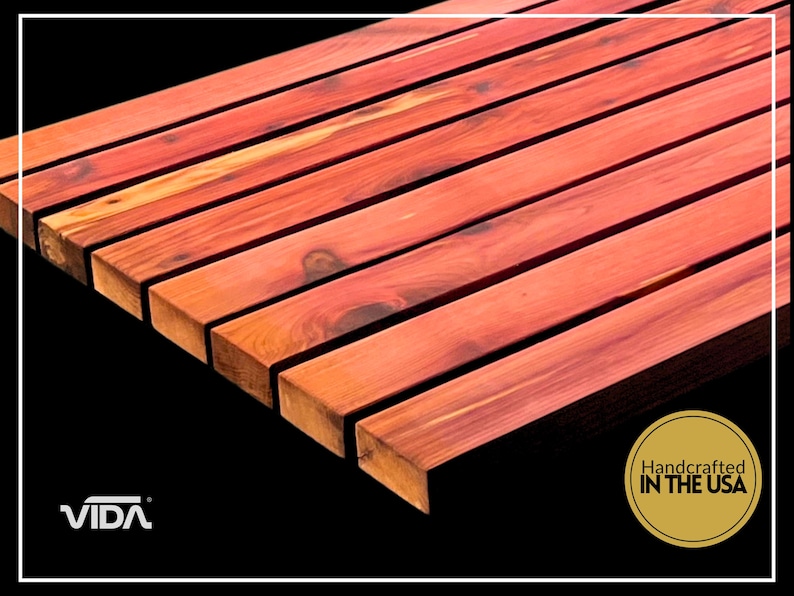 May include: A series of parallel, reddish-brown cedar wood slats arranged horizontally. The wood features visible natural grain patterns and knots. A logo with the text VIDA and a circular gold seal stating Handcrafted IN THE USA are visible.