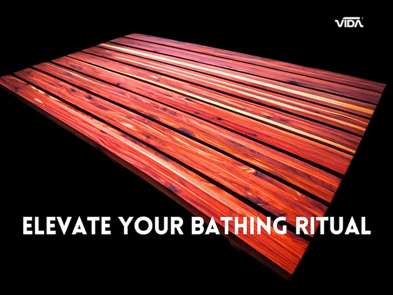 May include: A rectangular bath mat constructed from parallel slats of reddish-brown wood with visible grain patterns. The text VIDA appears in the top right corner, and the text ELEVATE YOUR BATHING RITUAL is printed in white at the bottom.