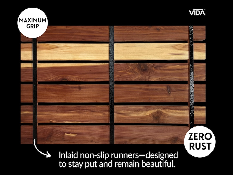 May include: A rectangular wooden bath mat composed of horizontal cedar slats in varying shades of brown and tan, secured by two vertical black non-slip runners. The mat features text labels reading MAXIMUM GRIP, ZERO RUST, VIDA, and Inlaid non-slip runners.