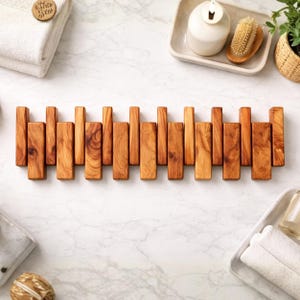 May include: A wooden coat rack for wall mounting, featuring a series of vertical wooden slats of different heights. The rack is made of light brown wood with visible grain patterns. The design is minimalist and suitable for a bathroom or hallway.