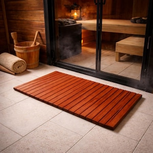 May include: A rectangular wooden floor mat constructed from parallel slats of reddish-brown wood. The mat features a smooth, flat surface with narrow gaps between each individual wooden plank, designed for placement on a tiled floor surface.