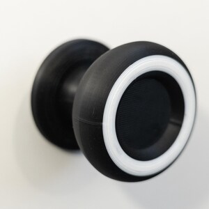 May include: A black and white door knob with a circular design. The knob has a black body with a white ring around the edge. The knob is mounted on a white surface.