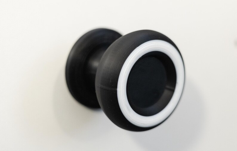 May include: A black and white door knob with a circular design. The knob has a black body with a white ring around the edge. The knob is mounted on a white surface.