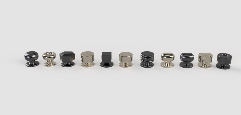 May include: A selection of ten cabinet knobs in diverse shapes and finishes. The knobs feature round, faceted, and cylindrical designs in metallic colours such as black, silver, and gold. They are arranged in a row against a white backdrop.