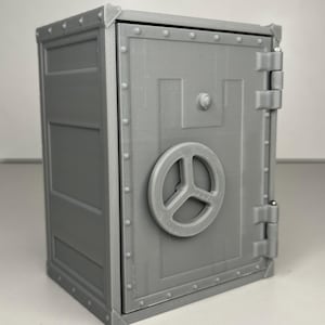 May include: A gray, miniature safe with a round handle on the door. The safe has a rectangular shape with riveted edges and a hinged door. The overall design is industrial and secure, suggesting a storage theme.