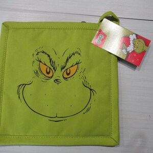 May include: A lime green square pot holder featuring a black and yellow cartoon face. The pot holder has a loop for hanging and a tag with a cartoon image. The pot holder is a kitchen accessory.