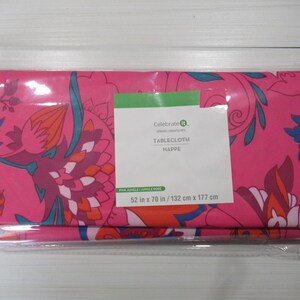 May include: A folded pink tablecloth with a floral pattern in shades of blue, orange, and purple. The label reads "TABLECLOTH HAPPE" and indicates dimensions of 52 in x 70 in (132 cm x 177 cm).